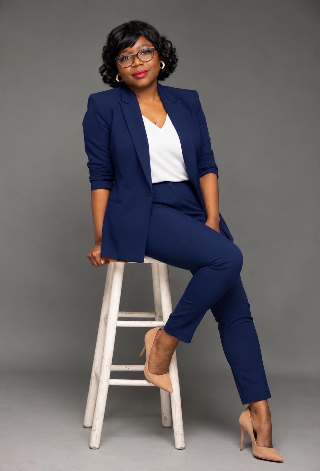 Misslath, en tailleur bleu nuit, assise sur un tabouret